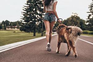 They both love jogging. Close-up rear view of young woman running with her dog through the park while spending time outdoors photo