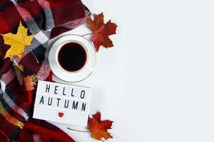 cálida tela escocesa a cuadros y una taza de café espresso caliente sobre fondo blanco. hola concepto de otoño. hojas rojas caídas y bebida para el clima frío. foto