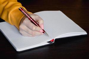 Woman writing in blank notebook. Close-up of hand holding pen. photo