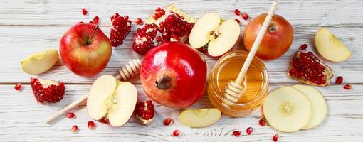 Rosh Hashanakh Jewish religious holiday. Banner format. Apples, pomegranates and honey on white wooden background. Traditional symbols photo