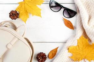 Hello autumn. Creative flat lay composition on white background. Yellow leaves, knitted sweater, backpack and glasses. photo