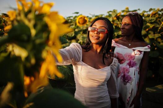 dos jóvenes amigas negras usan pose de vestido de verano en un campo de girasoles. foto