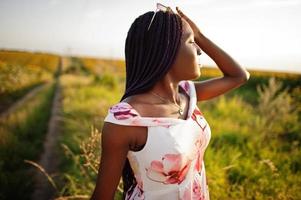 una mujer negra muy joven usa una pose de vestido de verano en un campo de girasoles. foto