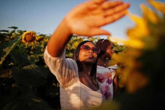 dos jóvenes amigas negras usan pose de vestido de verano en un campo de girasoles. foto