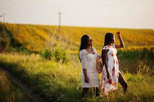 Two pretty young black friends woman wear summer dress pose in a sunflower field. photo