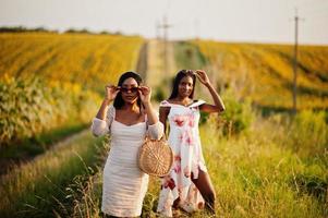 dos jóvenes amigas negras usan pose de vestido de verano en un campo de girasoles. foto