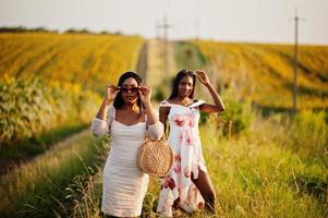 Two pretty young black friends woman wear summer dress pose in a sunflower field. photo