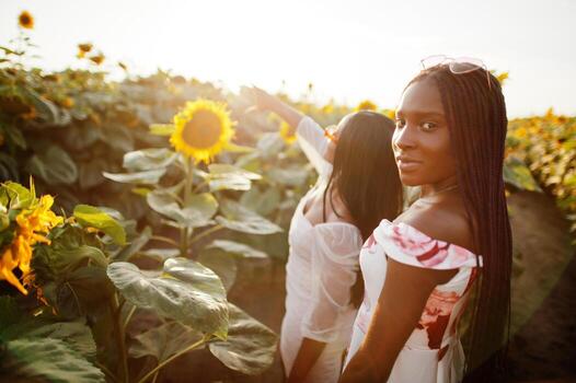 dos jóvenes amigas negras usan pose de vestido de verano en un campo de girasoles. foto