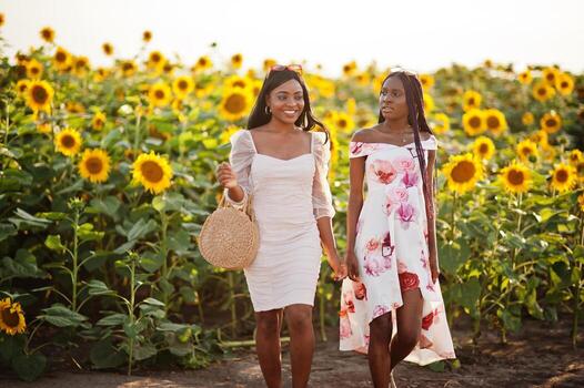 dos jóvenes amigas negras usan pose de vestido de verano en un campo de girasoles. foto
