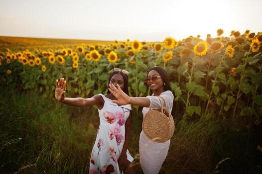 dos jóvenes amigas negras usan pose de vestido de verano en un campo de girasoles. foto