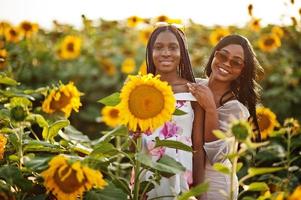 dos jóvenes amigas negras usan pose de vestido de verano en un campo de girasoles. foto