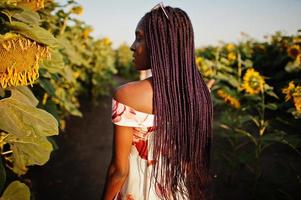 una mujer negra muy joven usa una pose de vestido de verano en un campo de girasoles. foto