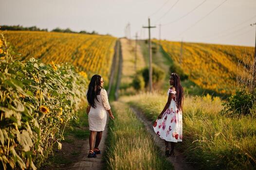 dos jóvenes amigas negras usan pose de vestido de verano en un campo de girasoles. foto