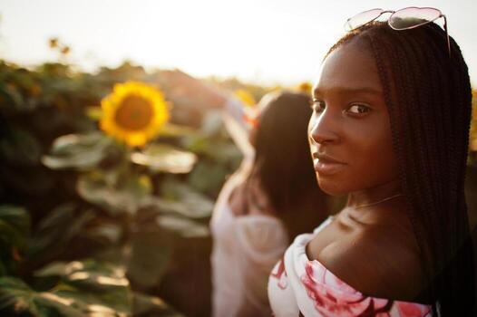 dos jóvenes amigas negras usan pose de vestido de verano en un campo de girasoles. foto