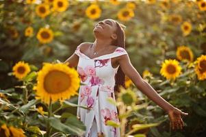 Pretty young black woman wear summer dress pose in a sunflower field. photo