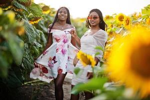 Two pretty young black friends woman wear summer dress pose in a sunflower field. photo