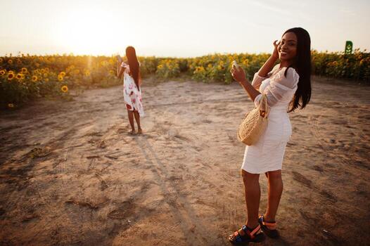 dos jóvenes amigas negras usan pose de vestido de verano en un campo de girasoles. foto