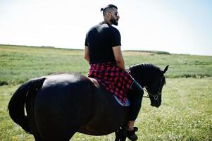 El hombre árabe de barba alta usa un caballo árabe negro. foto