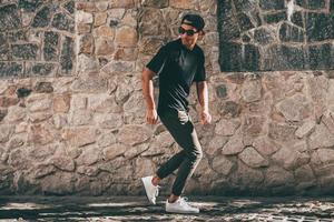 Young and carefree. Full length of handsome young African man in casual clothes moving and gesturing while standing against the stoned wall outdoors photo