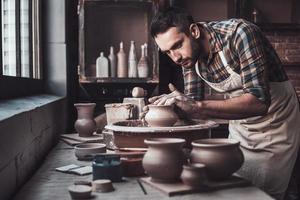 Total concentration at work. Confident young man making ceramic pot on the pottery wheel photo