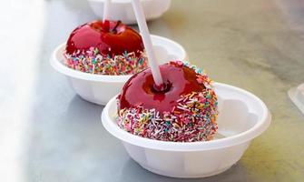 A red caramelized apple on a stick, covered in hard red sugar, standing in a plastic plate to serve as a festive treat. The concept of Easter, Maslenitsa,Valentine's Day photo