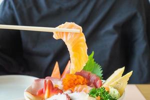 Salmon slice in chopsticks, Eating Sashimi Rice Bowl Chirashi Don Japanese food photo