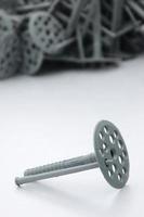 A gray plastic dowel fastening for thermal insulation with round umbrella caps lies on a gray foam polystyrene plate photo