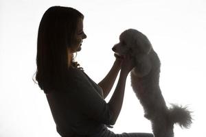 oscuro silueta de un niña con un bichón perrito en un blanco antecedentes. foto