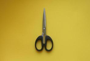 Black stainless steel scissors isolated photo on yellow background. School or office tools equipment object.