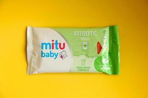 West Jakarta, Indonesia - February 10th, 2023 - Travel size tisu basah baby wipes green food grade in small plastic packaging. Hygiene product for children. Photo isolated on yellow background.