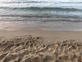 Seashore where the sand meets the water. In the sand there are footprints of human feet. photo