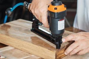 carpenter using nail gun or brad nailer tool on wood box in a workshop ,furniture restoration woodworking concept. selective focus photo