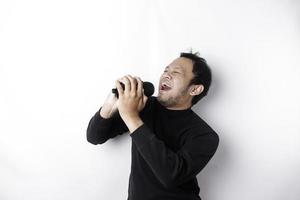 Portrait of carefree Asian man, having fun karaoke, singing in microphone while standing over white background photo