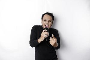 Portrait of carefree Asian man, having fun karaoke, singing in microphone while standing over white background photo