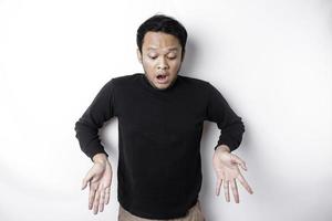 Shocked Asian man wearing black shirt, pointing at the copy space below him, isolated by white background photo