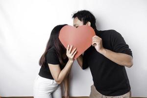 un Pareja en amor sostiene un papel rojo corazón, cubierta su caras. contento San Valentín día foto