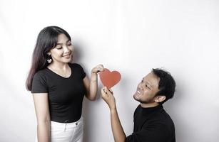 A young Asian couple smiling and holding red heart-shaped paper, isolated by white background photo