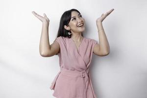 Excited Asian woman dressed in pink, pointing at the copy space on top of her, isolated by white background photo