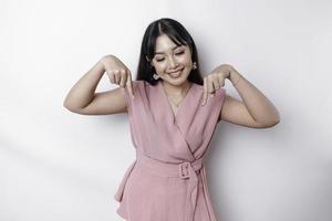 Excited Asian woman dressed in pink, pointing down at the copy space, isolated by white background photo