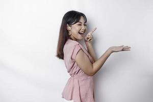 Excited Asian woman dressed in pink, pointing at the copy space beside her, isolated by white background photo