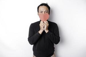 asiático hombre participación un rojo papel corazón forma cubierta su rostro. enamorado concepto foto