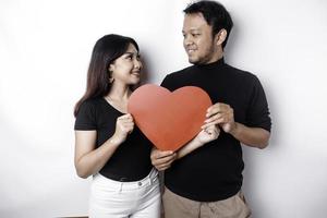 A young Asian couple smiling and holding red heart-shaped paper, isolated by white background photo