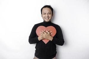 un retrato de un contento asiático hombre vistiendo un negro camisa, participación un rojo en forma de corazon papel aislado por blanco antecedentes foto