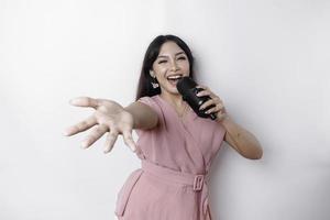 Portrait of carefree Asian woman, having fun karaoke, singing in microphone while standing over white background photo