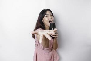 Portrait of carefree Asian woman, having fun karaoke, singing in microphone while standing over white background photo