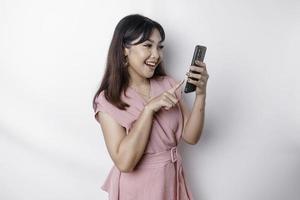 A portrait of a happy Asian woman dressed in pink and holding her phone, isolated by white background photo