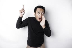 Shocked Asian man wearing black shirt pointing at the copy space on top of him, isolated by white background photo