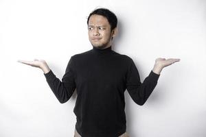 A portrait of an Asian man wearing a black shirt looks so confused between choices, isolated by a white background photo