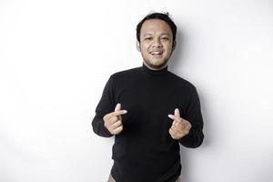 A happy young Asian man wearing a black shirt feels romantic shapes heart gesture expressing tender feelings photo