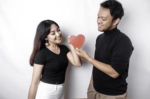A young Asian couple smiling and holding red heart-shaped paper, isolated by white background photo